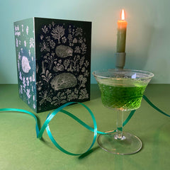 Lush Designs hedgehog print card ith a glass of green drink and a candle